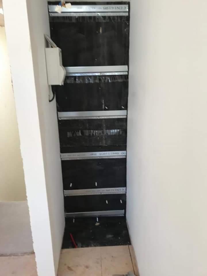 Montaż stelaża z profili aluminiowych i czarnej izolacji na ścianie, przygotowanie do montażu okładziny.