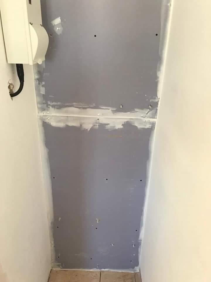 Ściana z zamontowanymi płytami, widoczne ślady szpachlowania łączeń i otworów po wkrętach, obok biała ściana i narożnik z instalacją elektryczną.