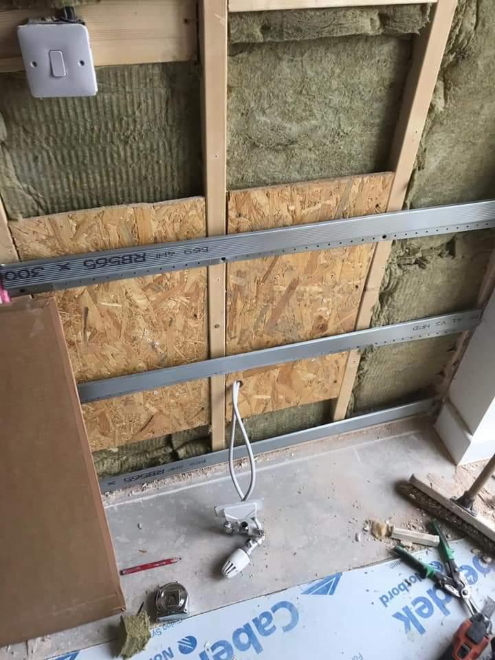 Montaż izolacji z wełny mineralnej i konstrukcji metalowej pod okładzinę sufitową, widoczne narzędzia i przewód elektryczny.