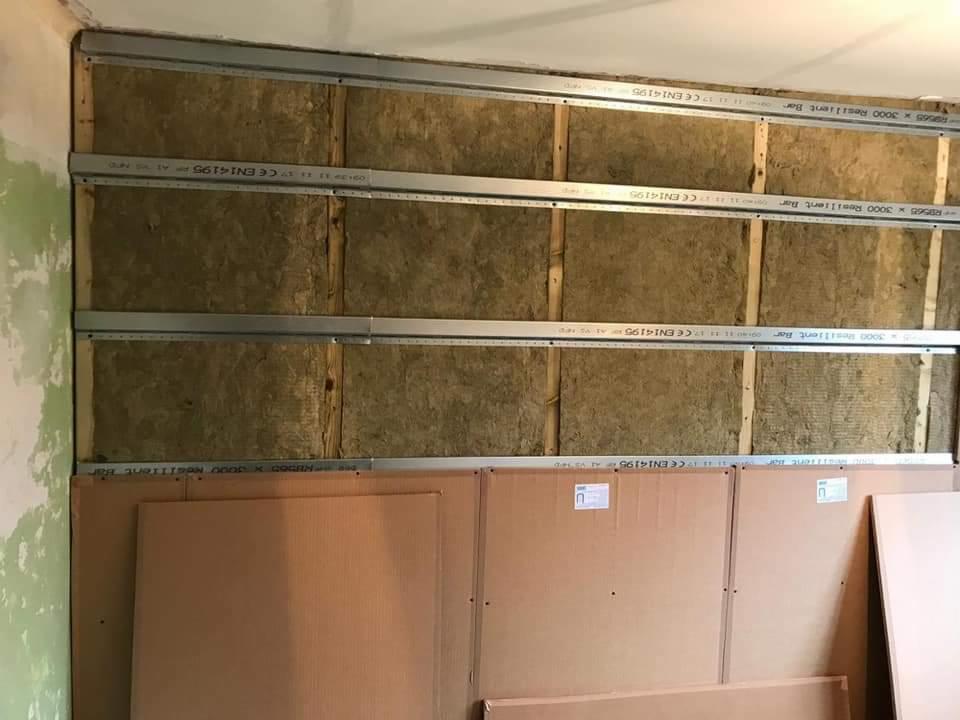 Montaż płyty karton gips: widoczne profile metalowe, wełna mineralna jako izolacja oraz płyty karton gips przed montażem na ścianie.