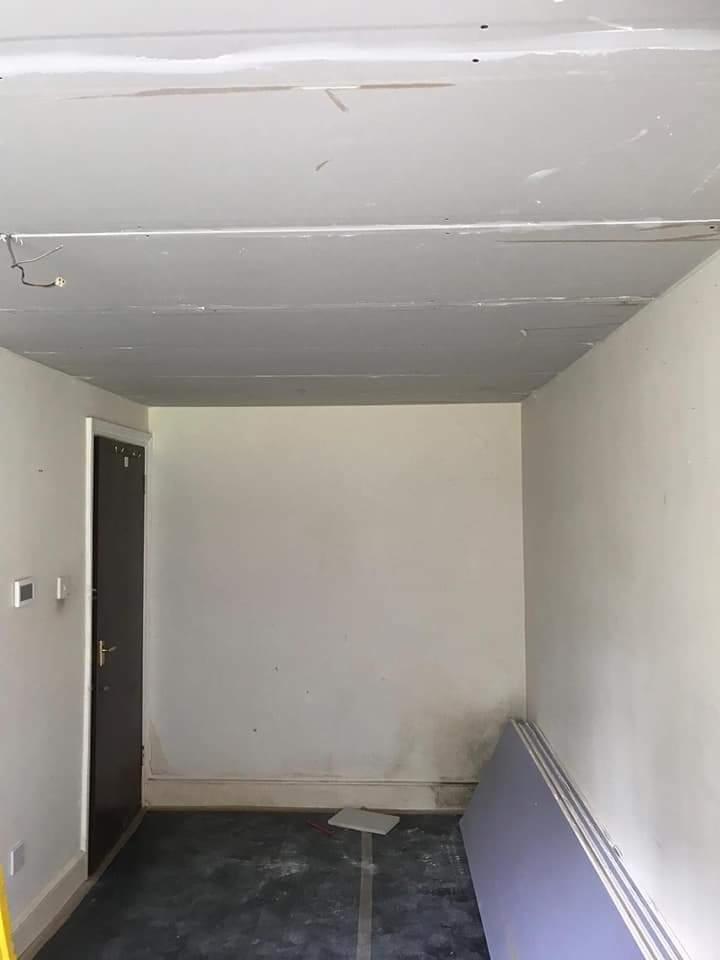 Pokój w trakcie remontu: sufit z zamontowanymi płytami, widoczne łączenia wymagające wykończenia, ściany przygotowane do malowania, kilka płyt opartych o ścianę w rogu pomieszczenia.