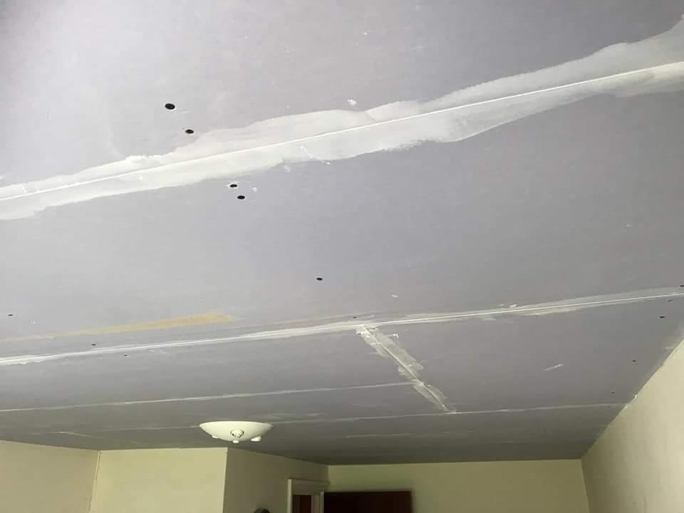 Szpachlowana powierzchnia sufitu z widocznymi łączeniami płyt i punktowymi otworami, przygotowana do dalszego wykończenia, z zamontowaną lampą sufitową.