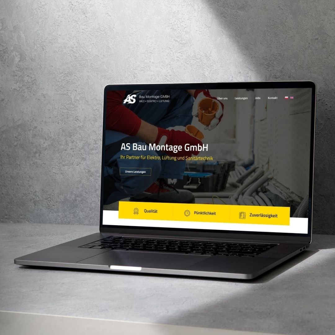 Laptop prezentuje stronę internetową AS Bau Montage GmbH z Tarnowa, oferującą usługi elektro, wentylacji i sanitarne. Żółty pasek z ikonami: jakość, punktualność, niezawodność.