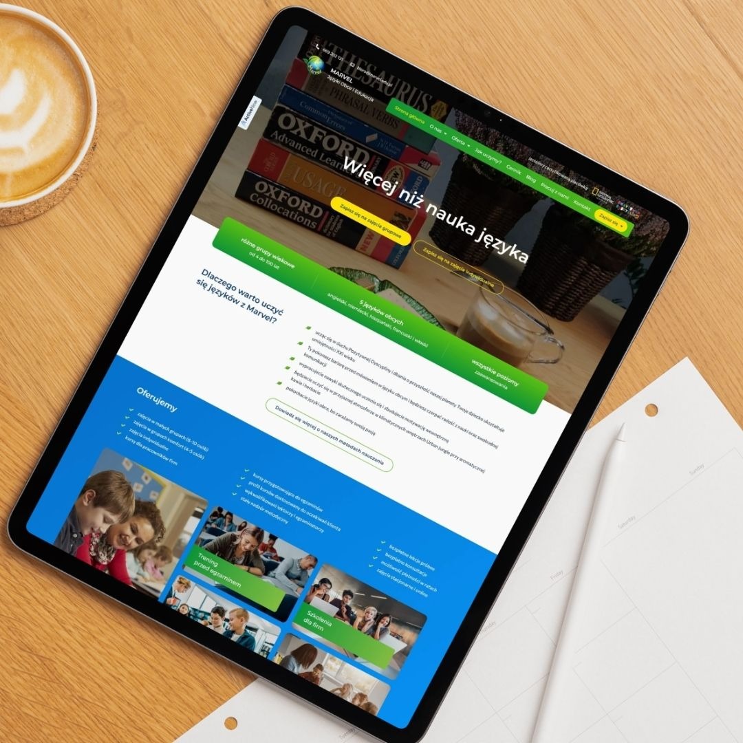 Tablet prezentuje stronę internetową szkoły językowej Marvel z ofertą kursów. Widoczne książki, kawa i kalendarz na drewnianym biurku. Jasne, naturalne światło.