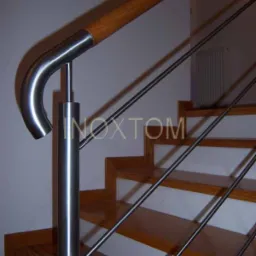 Nowoczesne schody drewniane z balustradą ze stali nierdzewnej i drewnianym pochwytem, widoczne mocowania linkowe, w tle grzejnik.