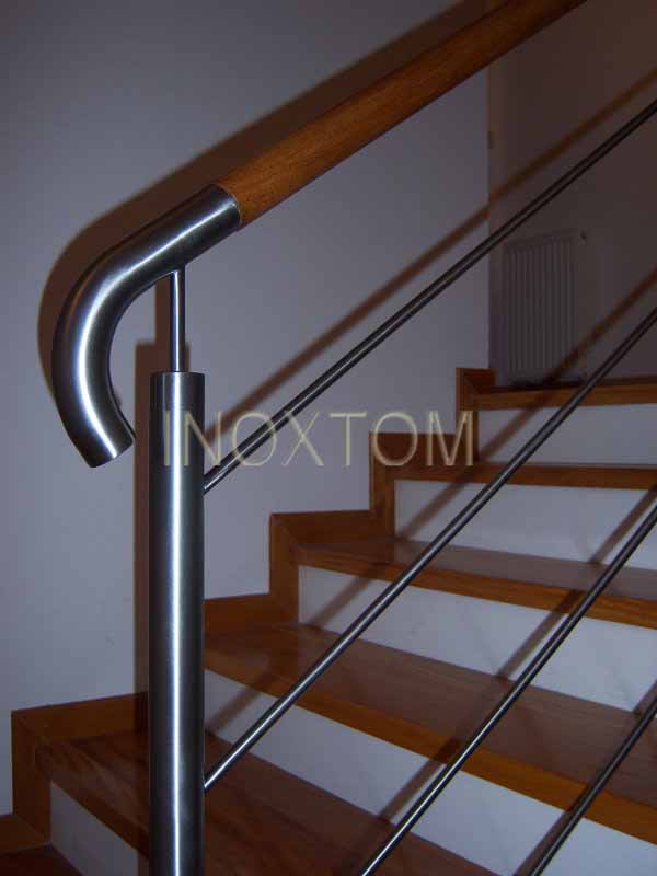 Nowoczesne schody drewniane z balustradą ze stali nierdzewnej i drewnianym pochwytem, widoczne mocowania linkowe, w tle grzejnik.