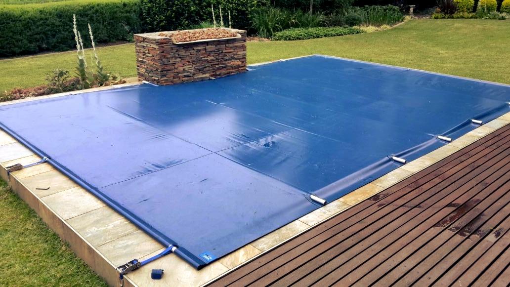 Zabezpieczony niebieską plandeką basen w ogrodzie w Zielonej Górze, z kamienną dekoracją obok.