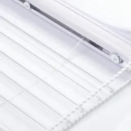 Detaliczne ujęcie białych, transparentnych żaluzji z mechanizmem łańcuszkowym na jasnym tle.