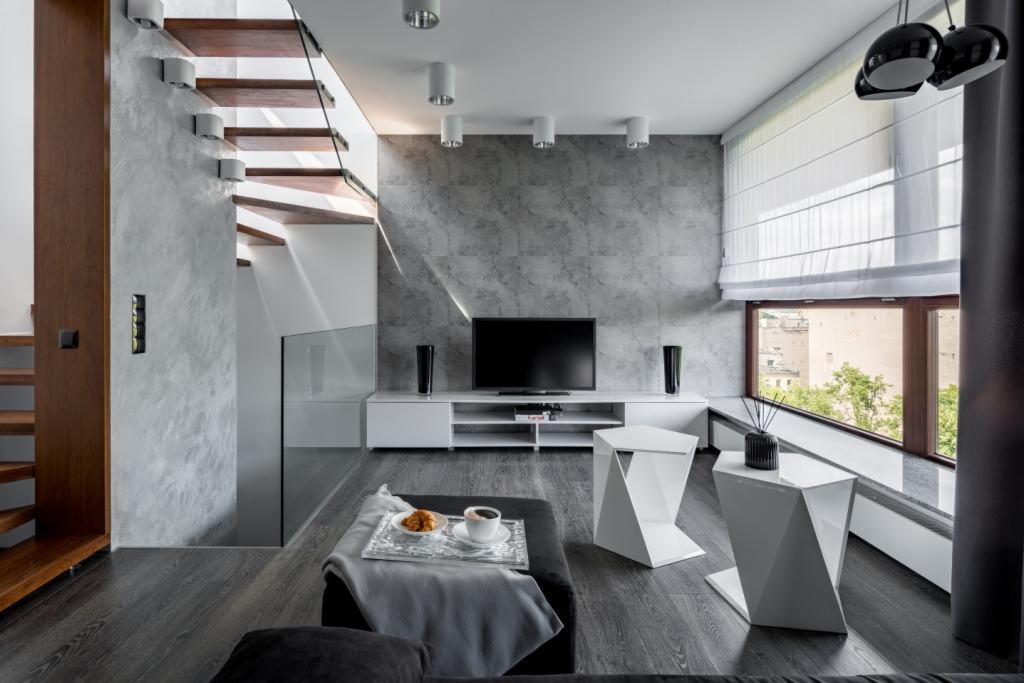 Nowoczesny salon z białymi roletami rzymskimi, drewnianymi schodami i szarą ścianą z telewizorem.