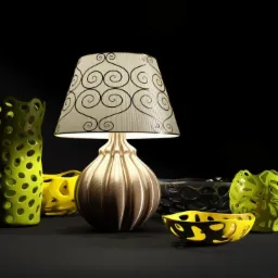 Beżowa lampka nocna z abażurem w spiralne wzory, otoczona dekoracyjnymi wazonami i misami z ażurowymi wycięciami w odcieniach zieleni, żółci i czerni na ciemnym tle.