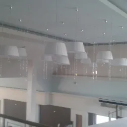 Wysoki sufit w dwupoziomowym pomieszczeniu z zamontowanymi białymi lampami z plisowanymi abażurami, ozdobionymi zwisającymi łańcuchami z kryształków.