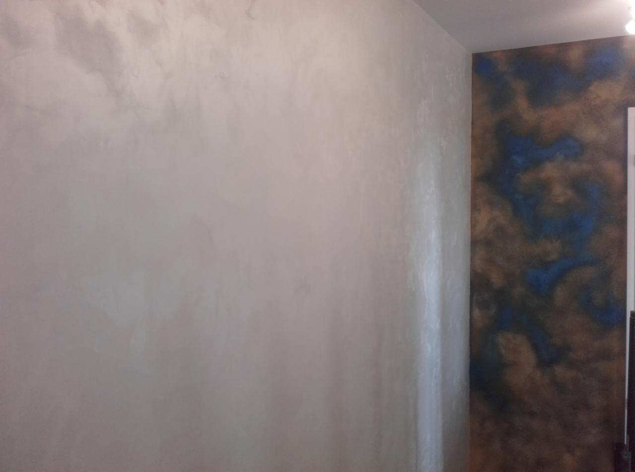 Ściana w mieszkaniu z dekoracyjną fakturą w odcieniach szarości i beżu, sąsiadująca z fragmentem ściany wykończonej farbą imitującą marmur w kolorach brązowym i niebieskim.