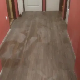 Ułożona podłoga z brązowych paneli imitujących drewno w korytarzu z pomalowanymi na czerwono ścianami i białymi drzwiami. Widoczne plastikowe krzyżyki dystansowe między panelami.