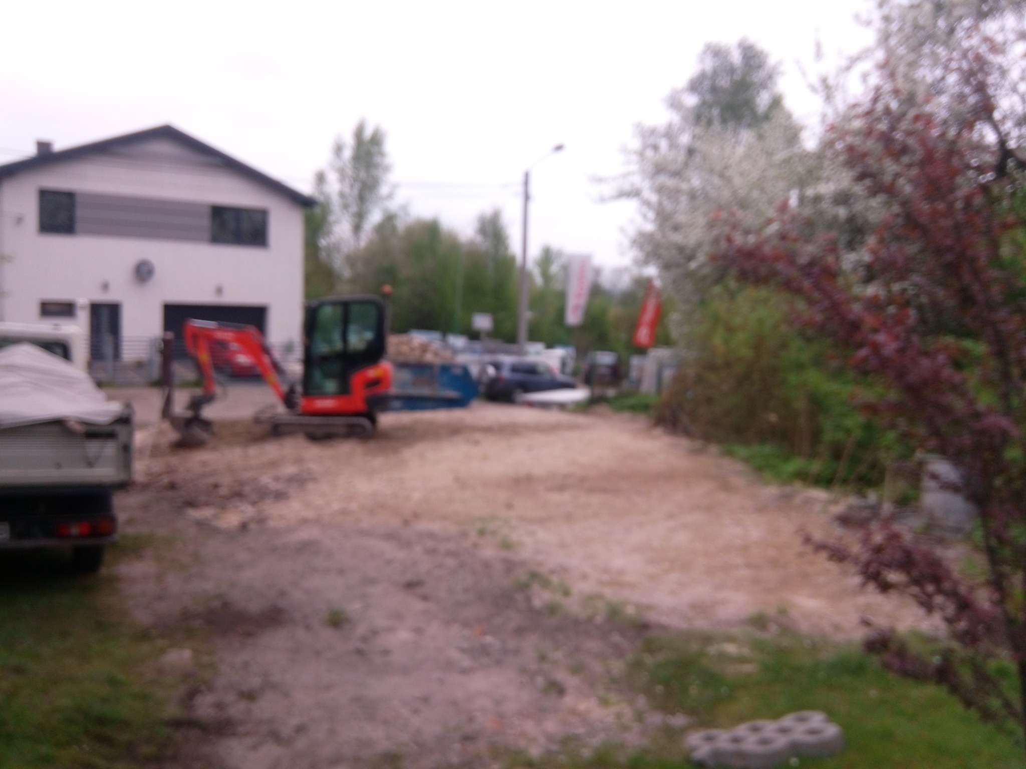 Mini koparka na placu budowy w Sosnowcu, widoczny kontener, gruz i budynek w tle, ujęcie zza zaparkowanego samochodu.