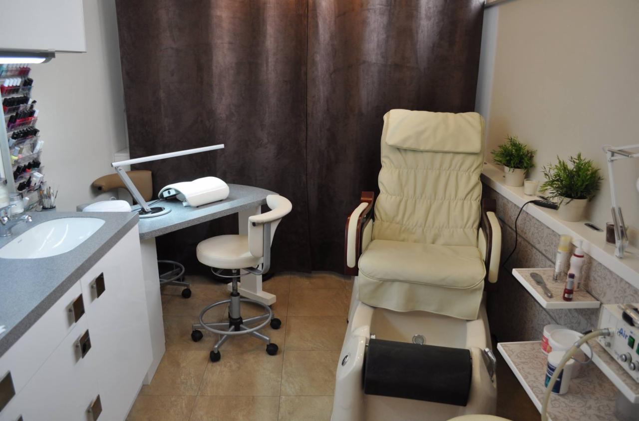 Salon kosmetyczny: fotel do pedicure z masażerem stóp, stanowisko do manicure z lampą UV i organizerem na lakiery, brązowe zasłony w tle.