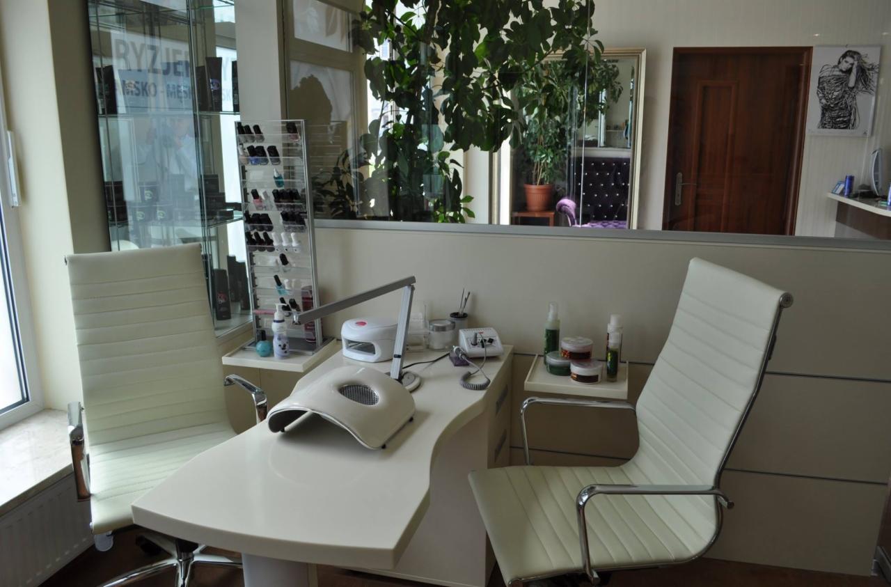 Stanowisko do manicure z lampą UV, frezarką i organizerem na lakiery w salonie kosmetycznym, widok z przodu na dwa krzesła obite białą skórą ekologiczną.