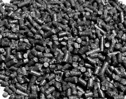 Duże zbliżenie na stos ciemnych, cylindrycznych bryłek opału, tekstura powierzchni chropowata, widoczne ślady obróbki, oświetlenie naturalne, czarno-biała fotografia.