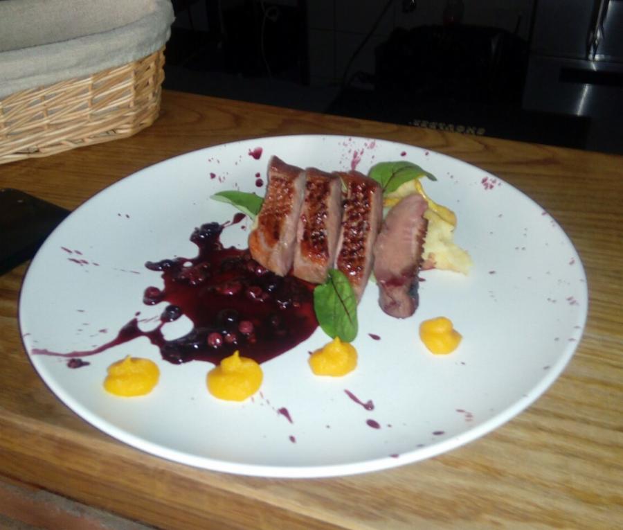 Elegancko podane plastry pieczonej kaczki z sosem jagodowym, puree dyniowym i dekoracją z listków na białym talerzu z efektem rozprysku farby.