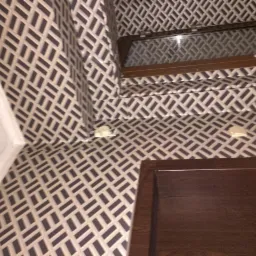 Ściana i sufit pokryte tapetą w geometryczny wzór, widoczne narożniki i fragment okna z drewnianą ramą.