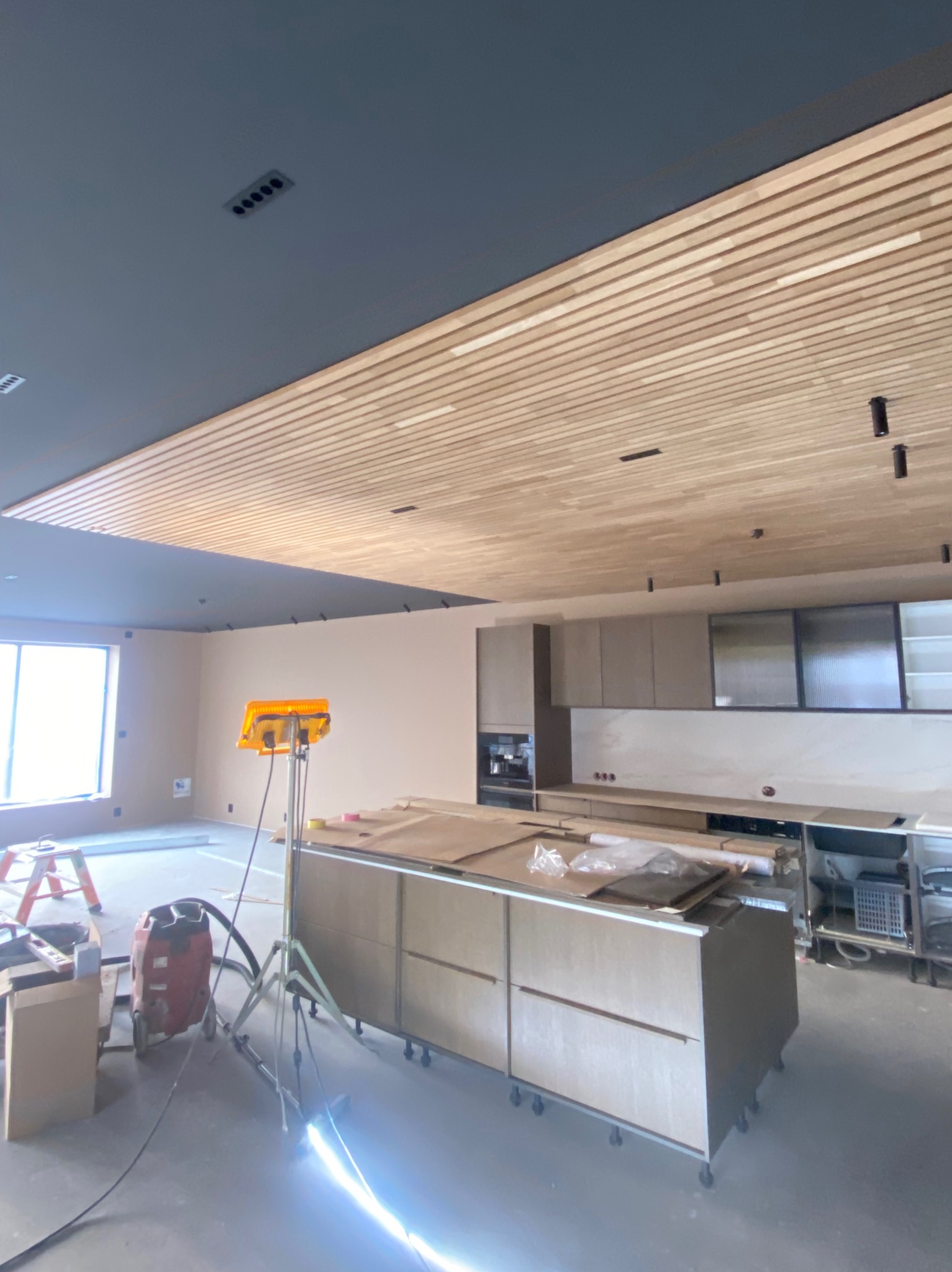 Montaż drewnianego sufitu lamelowego w nowoczesnej kuchni. Widoczny sprzęt budowlany i oświetlenie robocze. Częściowo zabudowa kuchenna w tle.
