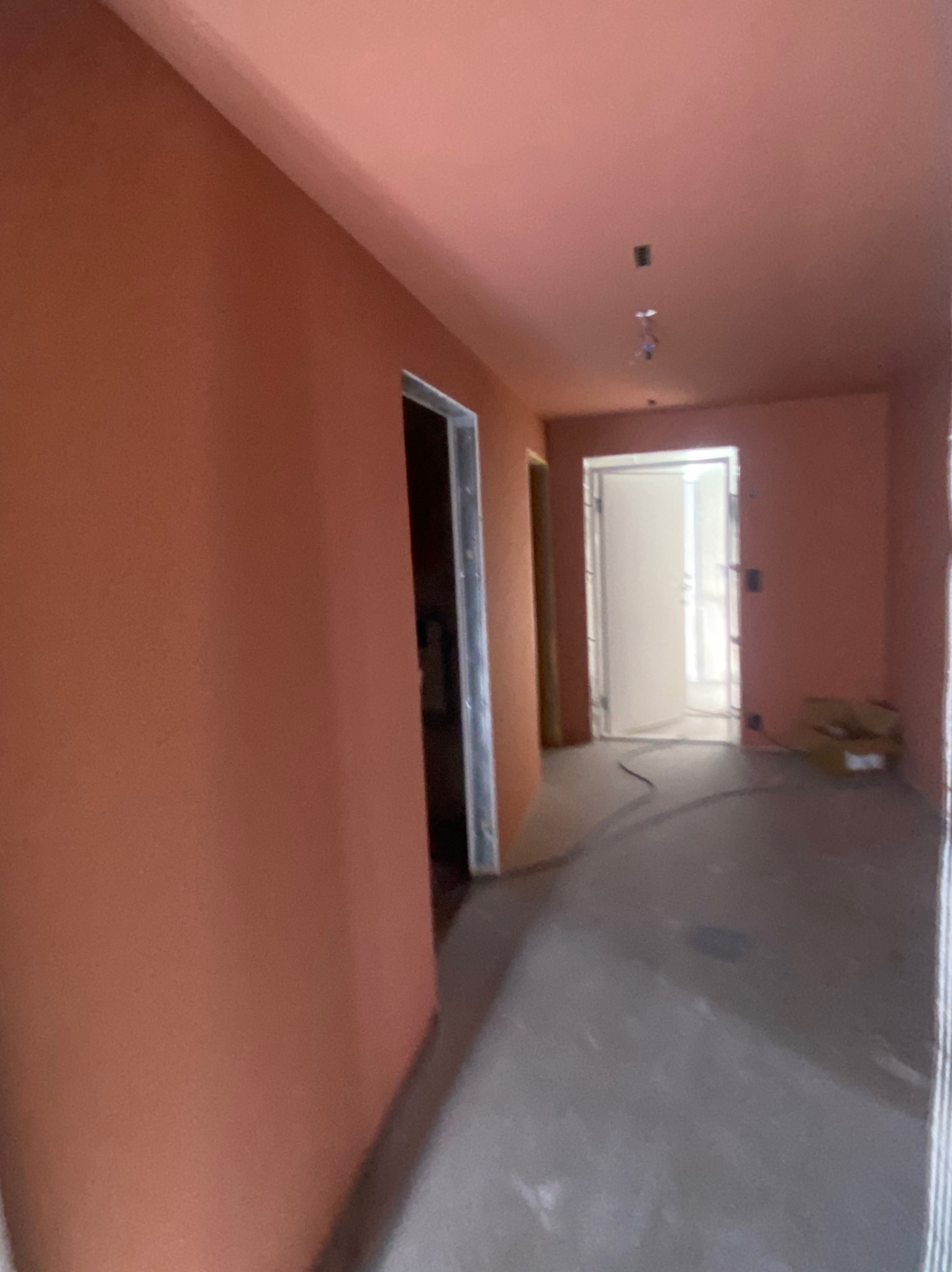 Pomarańczowe ściany i sufit w nowym mieszkaniu po malowaniu. Widoczne ościeżnice drzwi i podłoga w trakcie prac wykończeniowych. Ujęcie z perspektywy wnętrza.