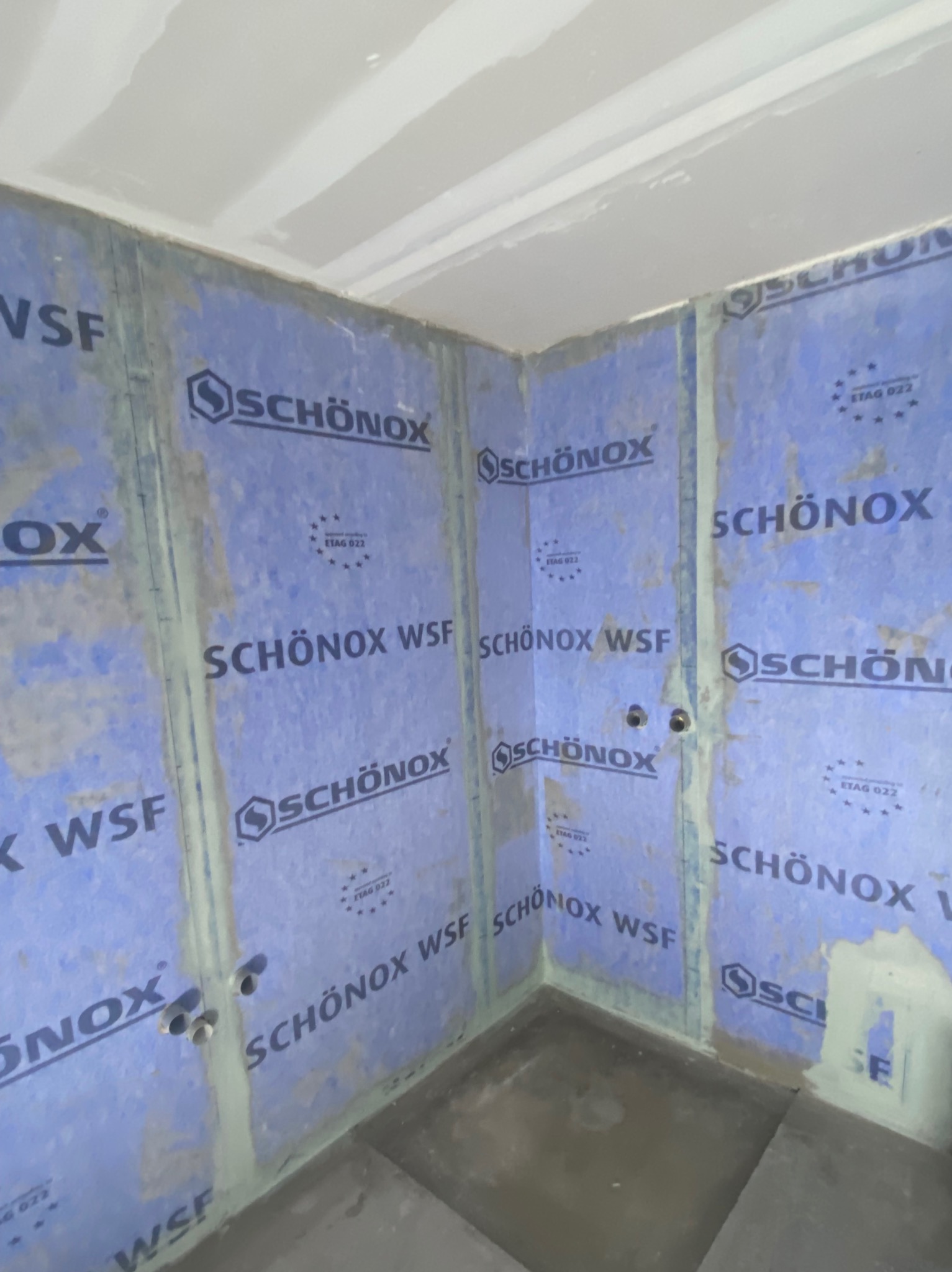 Montaż płyt uszczelniających marki Schönox Wsf w narożniku łazienki w Rybniku. Widoczne otwory na instalacje. Przygotowanie do dalszych prac wykończeniowych.