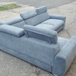 Szary narożnik tapicerowany z regulowanymi zagłówkami, ustawiony na betonowej nawierzchni.