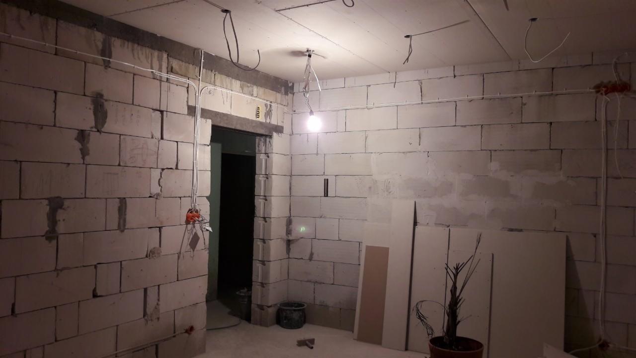 Surowy stan wnętrza w trakcie prac: ściany z betonu komórkowego, instalacja elektryczna w peszlach, przygotowane płyty gipsowo-kartonowe oparte o ścianę, surowa żarówka na kablu.
