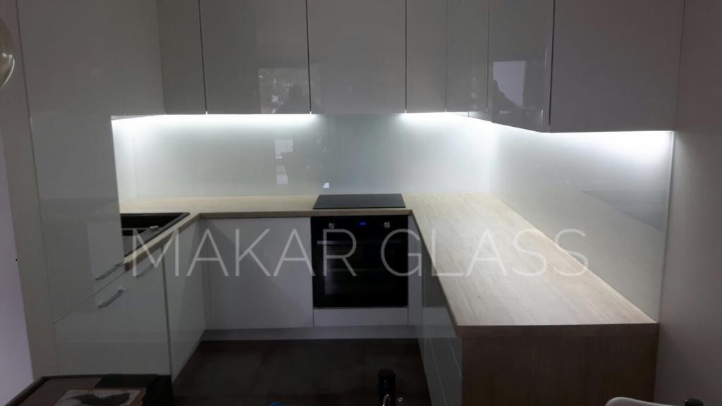 Nowoczesna kuchnia z białymi szafkami, szklanym panelem ściennym z podświetleniem LED i drewnianym blatem, prezentująca logo firmy 'MAKAR GLASS' nałożone na zdjęcie.