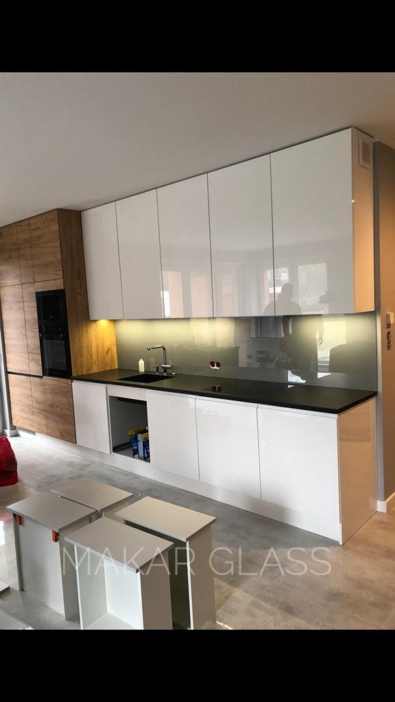 Montaż szklanej ściany nad blatem kuchennym z białymi szafkami i drewnianym panelem bocznym, widoczne elementy montażowe i niedokończone szafki dolne.