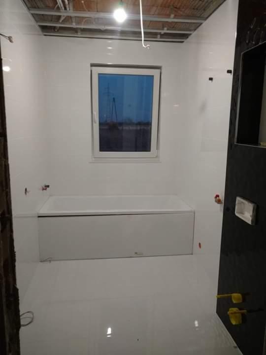 Biała łazienka w trakcie remontu: świeżo położone płytki podłogowe i ścienne, zamontowana wanna, widoczne niedokończone sufity i wystające kable.