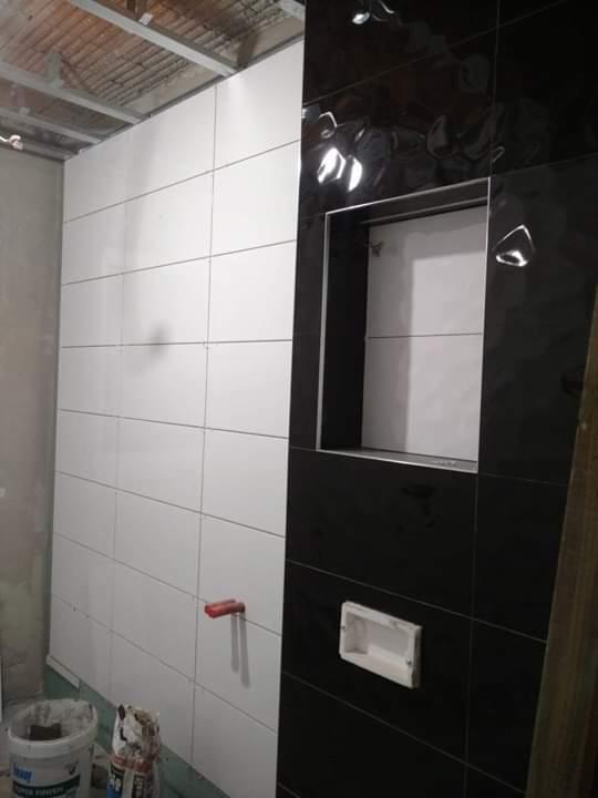 Ściana łazienki w trakcie wykańczania: białe i czarne, błyszczące płytki ceramiczne ułożone naprzemiennie, wnęka w czarnej ścianie, widoczne narzędzia i materiały budowlane na podłodze.