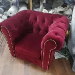 Bordowy fotel w stylu chesterfield z dekoracyjnymi gwoździami, widoczny na tle magazynu tkanin.