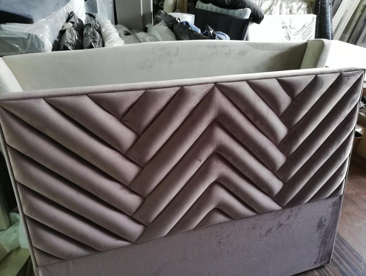 Fragment wezgłowia łóżka tapicerowanego w odcieniach pudrowego różu z geometrycznym wzorem chevron, widoczny w warsztacie.