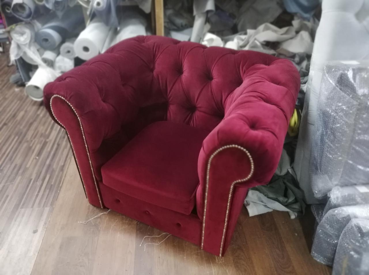 Bordowy fotel w stylu chesterfield z dekoracyjnymi gwoździami, widoczny na tle magazynu tkanin.
