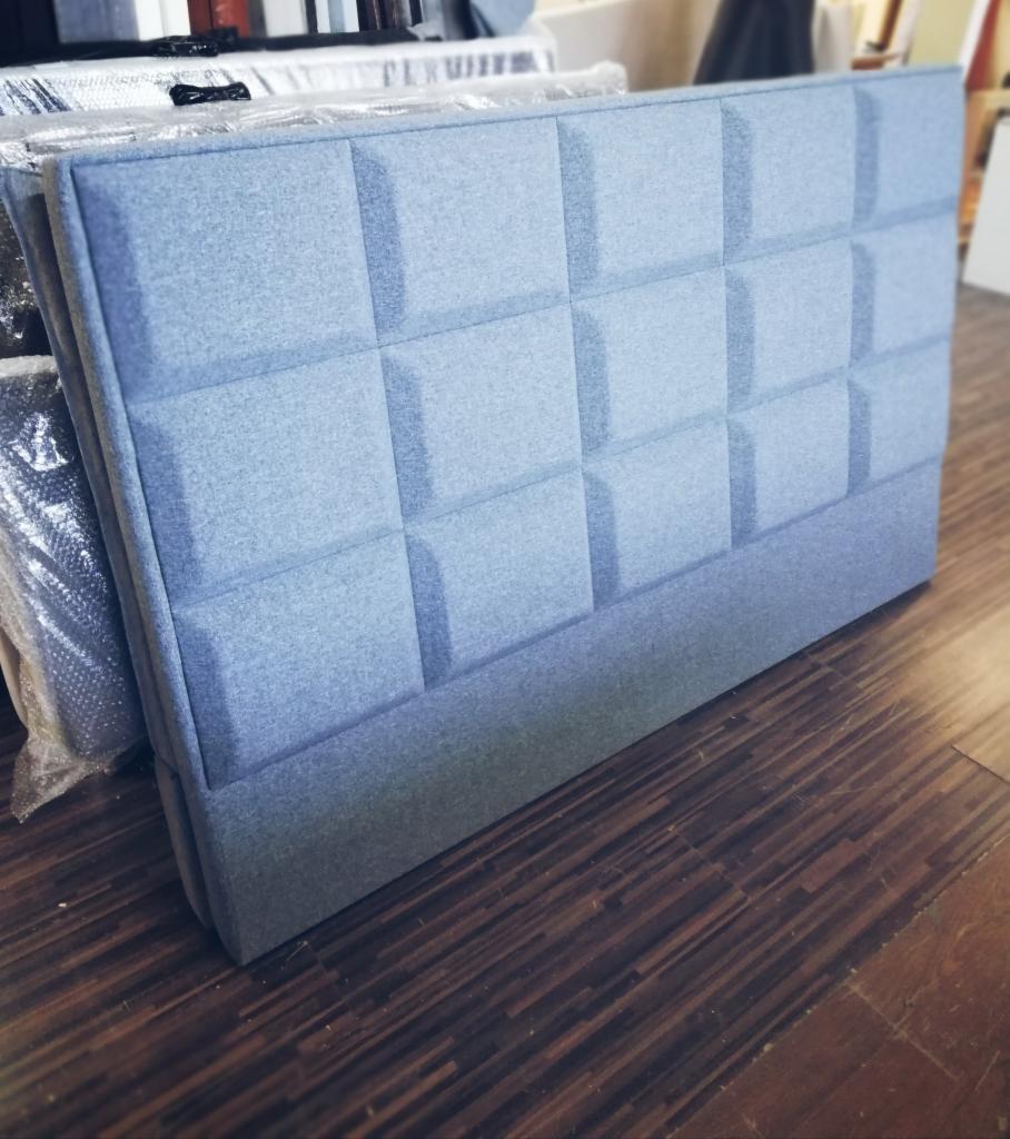 Błękitny, tapicerowany zagłówek z geometrycznym wzorem kwadratów, leżący na podłodze z paneli.