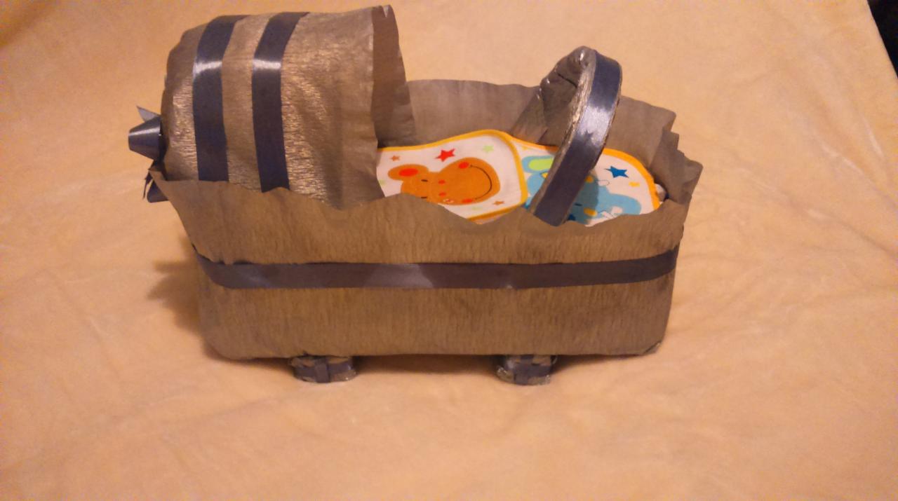 Ręcznie robiony kosz Mojżesza z tektury falistej i wstążki, zawierający dziecięce śliniaki z motywami zwierzęcymi.