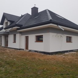 Piotr Jeż, MRÓWEX - Nowoczesny dom jednorodzinny z ciemną dachówką i jasną elewacją w pochmurny dzień. Widoczne detale wykończenia i otoczenie budynku.