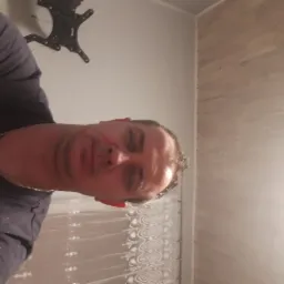 Mężczyzna robiący selfie na tle ściany z drewnianą okładziną i uchwytem do telewizora.