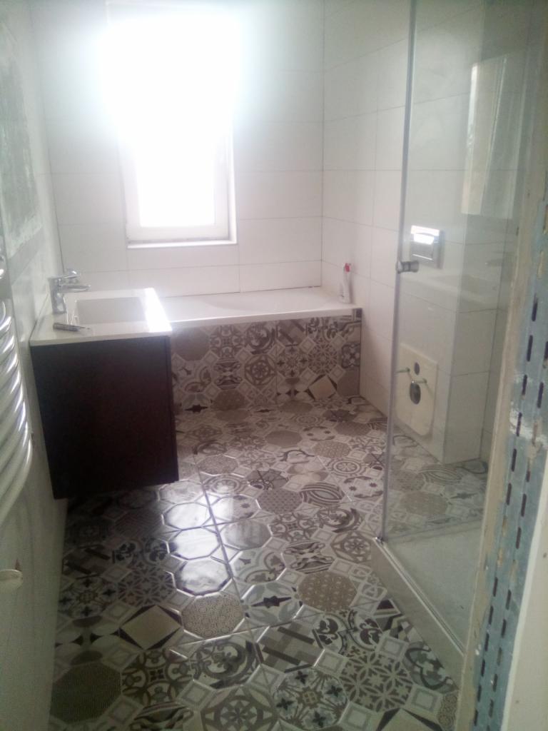 Jasna łazienka z mozaikową podłogą, zabudowaną wanną i umywalką z szafką, widok na kabinę prysznicową.