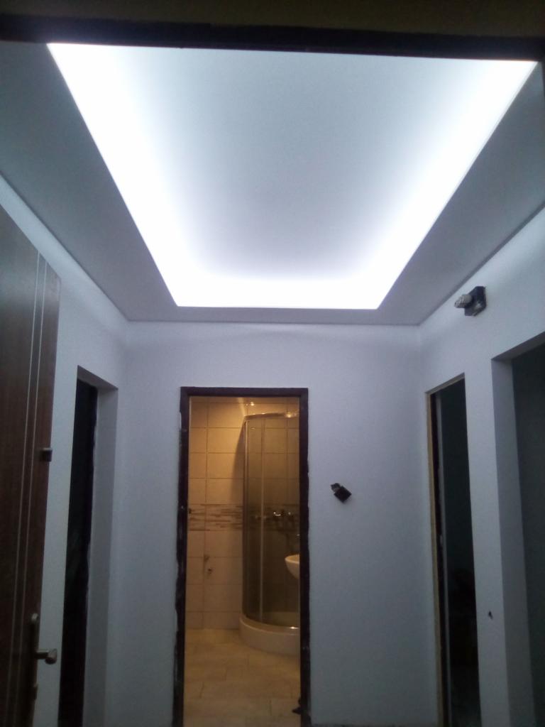 Nowoczesne oświetlenie sufitowe w korytarzu, widok na łazienkę z kabiną prysznicową.