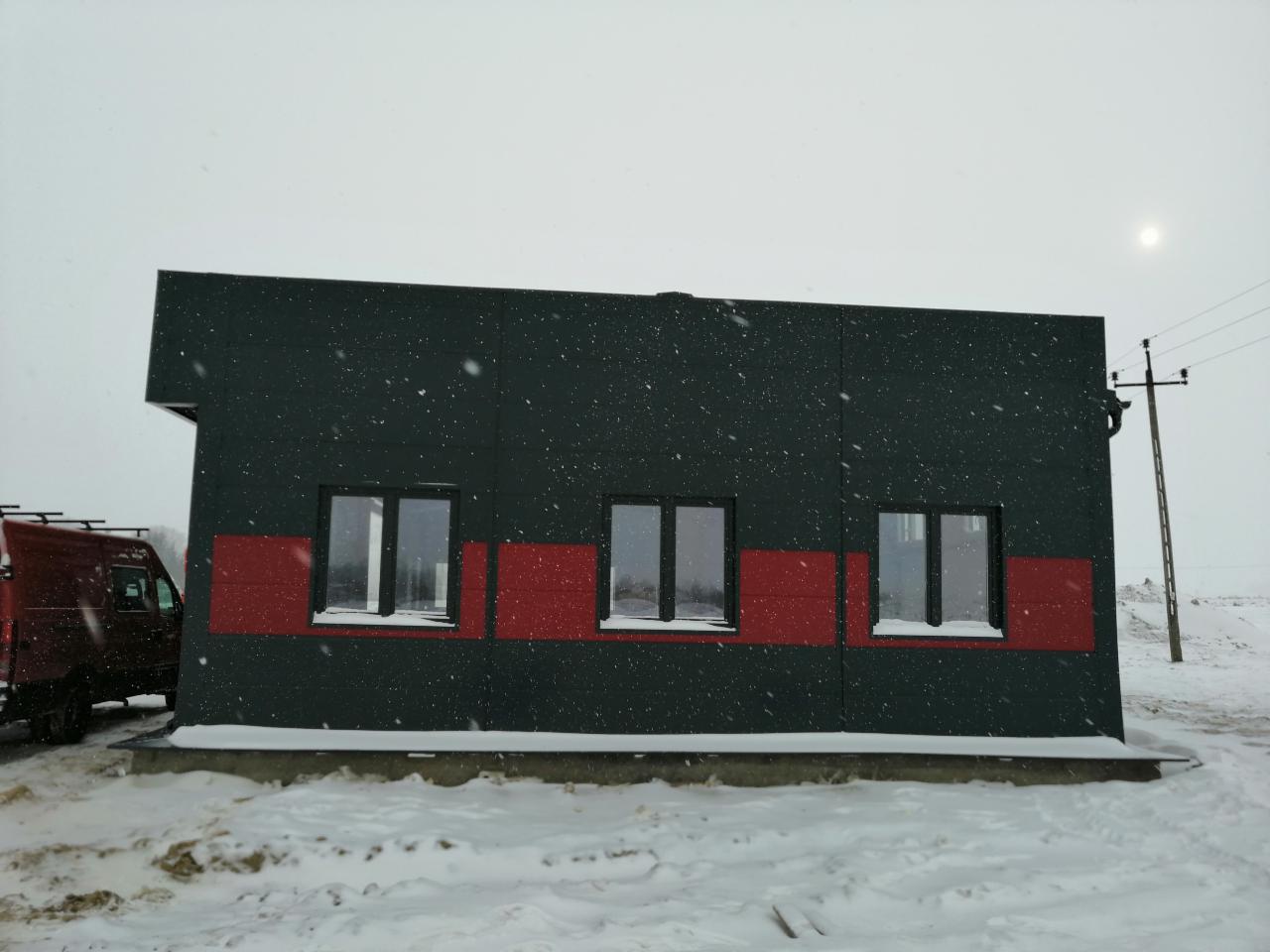 Gotowy budynek z płyt warstwowych w zimowej scenerii, widoczny samochód dostawczy z bagażnikiem dachowym.