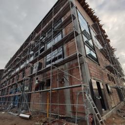 Salon Buderus TOP PARTNER - Budynek w trakcie montażu okien i elewacji, otoczony rusztowaniem, z widocznymi pracownikami na rusztowaniu.