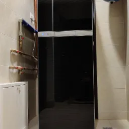 Czarny, nowoczesny piec grzewczy Buderus z podłączonymi rurami miedzianymi i dwoma zbiornikami wyrównawczymi (czerwony i niebieski) zamontowany w jasnej, wykafelkowanej łazience.