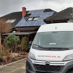 Salon Buderus TOP PARTNER - Dom jednorodzinny z panelami fotowoltaicznymi na dachu, na pierwszym planie biały samochód dostawczy z logo firmy NowyKociol.pl