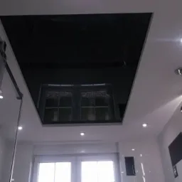 Nowoczesna łazienka z czarnym, błyszczącym sufitem napinanym, który odbija okno, oświetlenie punktowe i dekoracyjny żyrandol.