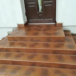 Wykończone płytkami schody wejściowe do domu w Limanowej, prowadzące do brązowych drzwi. Widoczne świeżo położone fugi między brązowymi płytkami.