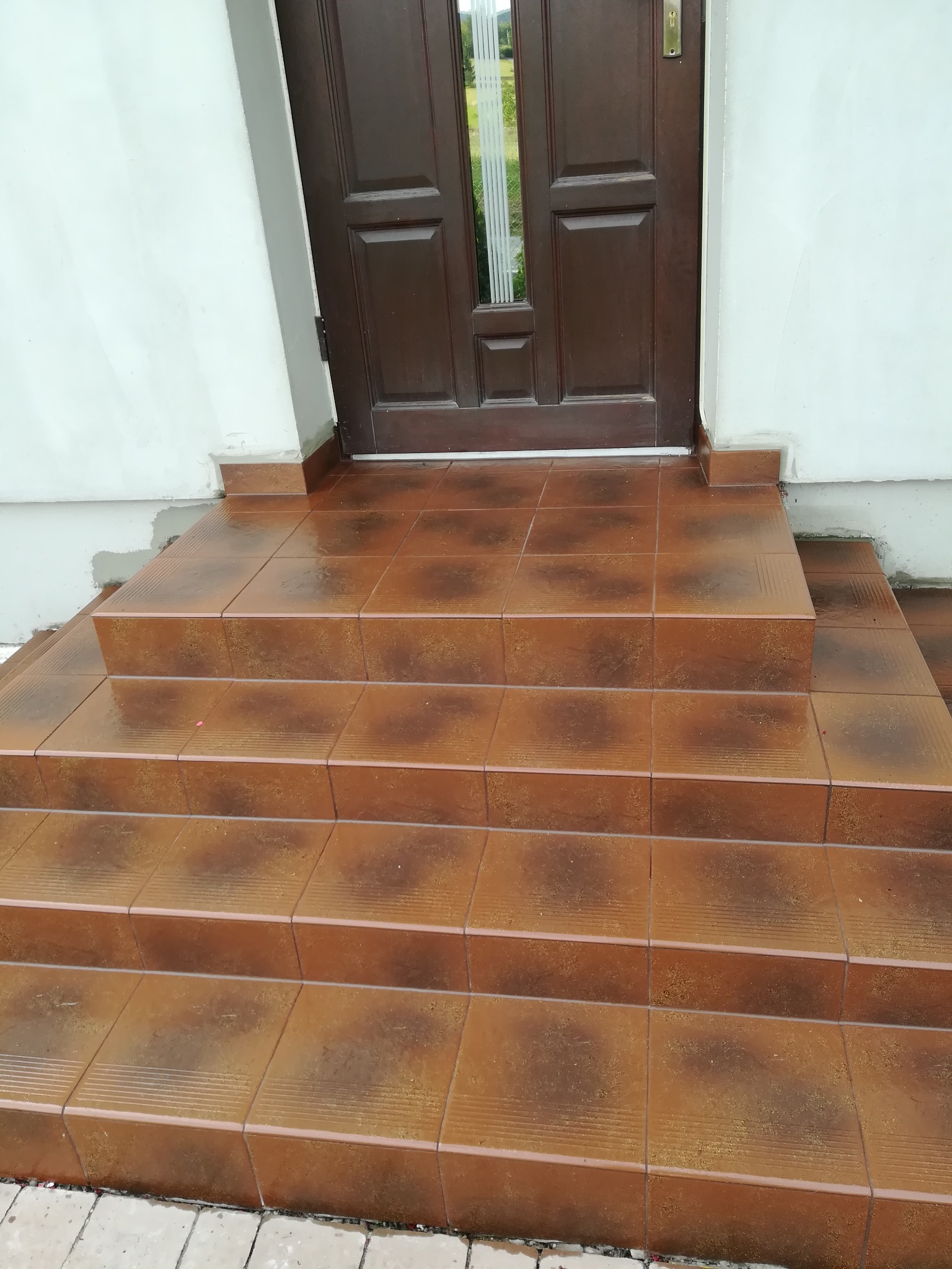 Wykończone płytkami schody wejściowe do domu w Limanowej, prowadzące do brązowych drzwi. Widoczne świeżo położone fugi między brązowymi płytkami.
