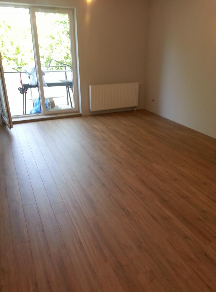 Nowo ułożona, brązowa podłoga z paneli w pustym pokoju z balkonem i białym grzejnikiem.