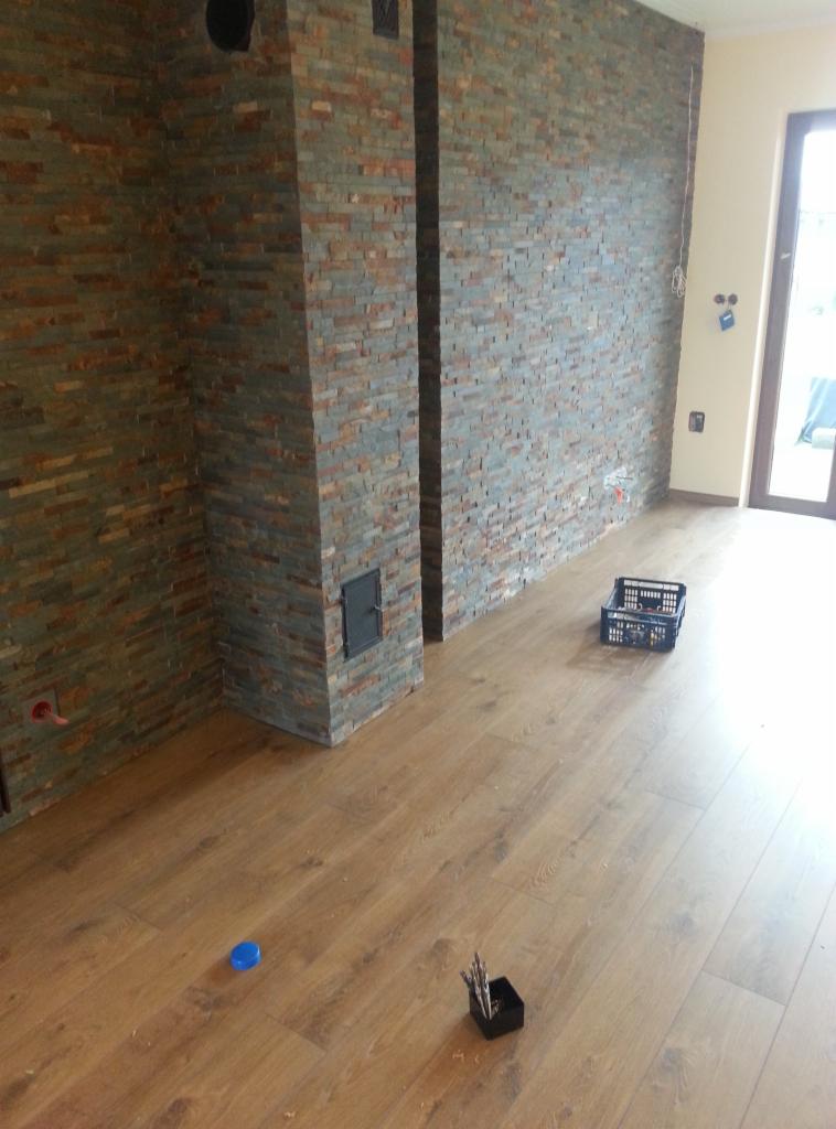 Wykończone wnętrze z okładziną ścienną z płytek imitujących kamień, drewnianą podłogą i narzędziami w rogu pokoju.